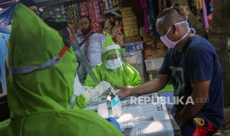 Petugas menggunakan alat pelindung diri (APD) lengkap melakukan tes diagnosa cepat (rapid test) pengunjung pasar. 