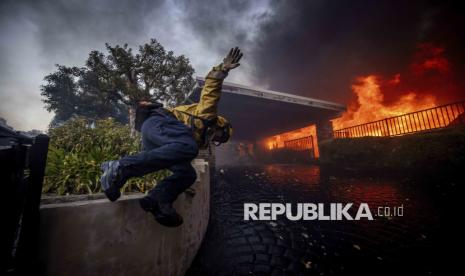 Petugas pemadam kebakaran melompati pagar saat berusaha memadamkan kebakaran besar yang melanda kawasan Pacific Palisades, Los Angeles, California, Selasa (7/1/2025) waktu setempat.