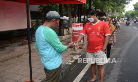 Panitia mengecek suhu yang warga mengantre untuk mengambil makanan berbuka puasa gratis 