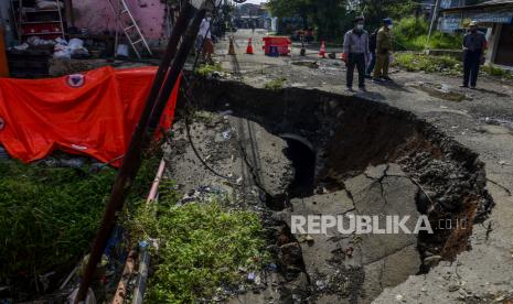 Petugas berdiri di dekat jalan yang longsor di Kampung Setu Asem, Mekarwangi, Tanah Sareal, Kota Bogor, Senin (10/5). Jalan yang longsor akibat hujan dengan intensitas deras dan tergerusnya pondasi tanah oleh aliran Kali Cigede Kulon. Bencana tersebut mengancam keselamatan tiga unit rumah warga hingga membuat jalan harus ditutup dari lalu lintas kendaraan. Republika/Putra M. Akbar