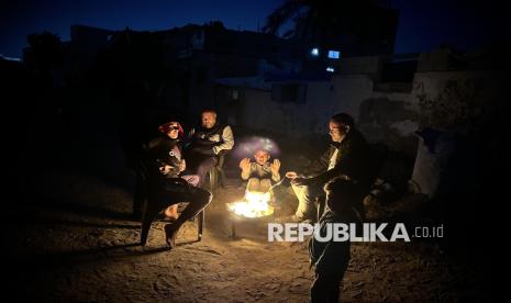 Keluarga Palestina berkumpul di sekitar api unggun untuk menghangatkan diri saat mengungsi di sebuah bangunan yang rusak, di Khan Yunis, Gaza, Rabu (4/12/2024). Sejumlah keluarga Palestina mengungsi di reruntuhan gedung yang hancur akibat serangan Israel. Mereka harus berjuang melawan kondisi cuaca dingin dan krisis pangan.