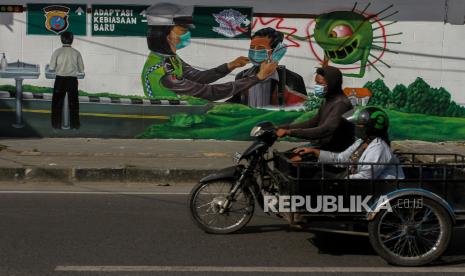 Pengendara becak bermotor melintas di depan mural bergambar Polwan memasangkan masker di Jalan Stasiun Kereta Api Medan, Sumatera Utara, Rabu (3/2/2021). Mural adaptasi kebiasaan baru karya anggota Komunitas Mural Medan ini dibuat sebagai bentuk edukasi sekaligus sosialisasi penerapan protokol kesehatan kepada warga untuk selalu memakai masker guna mencegah penyebaran COVID-19. 