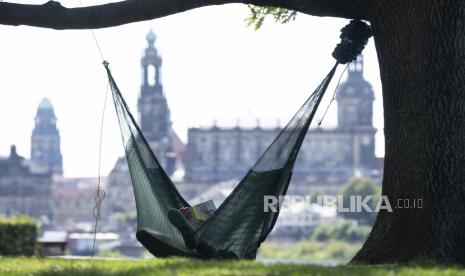  Seorang pria berbaring di tempat tidur gantung dan membaca buku di depan kota tua di Dresden, Jerman. Bloomsbury Publishing telah merevisi perkiraan keuntungannya untuk kedua kalinya tahun ini.