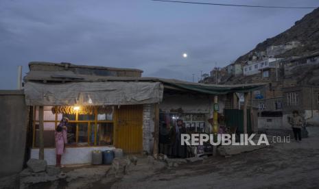 Seorang pemilik toko kelontong hijau Afghanistan berdiri di luar tokonya ketika seorang gadis membeli roti dari toko roti, di Kabul, Afghanistan, pada Rabu, 17 November 2021. 