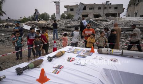 Warga melihat peluru mortir dan pecahan rudal Israel yang meledak saat mereka berdiri di puing-puing rumah yang hancur akibat serangan di Deir al-Balah, Jalur Gaza tengah. 