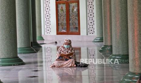  Seorang perempuan yang memakai masker sebagai antisipasi wabah virus Corona membaca kitab suci Alquran sambil menunggu waktu berbuka puasa di sebuah masjid. (ilustrasi)