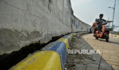 Warga mengendarai sepeda listrik melintas di dekat tanggul pengaman pantai yang retak di Kalibaru, Cilincing, Jakarta. Proyek pengaman pantai di Teluk Jakarta saat ini sudah mencapai 53,14 persen.