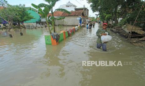 Warga berjalan menerobos banjir yang merendam Desa Suranenggala Lor, Kecamatan Suranenggala, Kabupaten Cirebon, Jawa Barat, Selasa (19/1/2021). Banjir akibat luapan sungai dan tingginya intensitas hujan di kawasan itu membuat ratusan rumah warga terendam banjir setinggi 50 sentimeter hingga satu meter. 