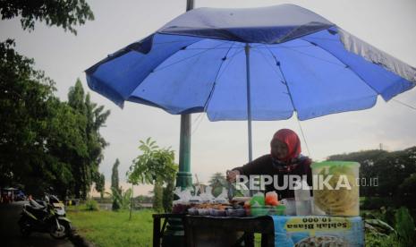 Pedagang takjil menggunakan payung untuk melindungi barang dagangannya dari hujan di kawasan Banjir Kanal Timur, Duren Sawit, Jakarta, Senin (27/3/2023). Badan Meteorologi Klimatologi dan Geofisika memprakirakan hujan masih berpotensi terjadi hingga awal April 2023 mendatang yang disebabkan dinamika atmosfer masih mengalami peralihan dari musim penghujan menuju musim kemarau.