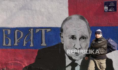 Seorang pria melewati mural yang menggambarkan Presiden Rusia Vladimir Putin, yang berbunyi: 