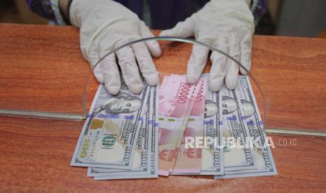 Petugas menunjukkan uang rupiah dan dolar AS di salah satu gerai penukaran mata uang asing. ilustrasi