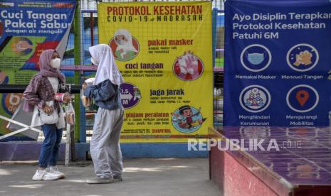 Sejumlah pelajar berbincang di depan spanduk tentang protokol kesehatan Covid-19 usai menjalani tes usap antigen di MI Cikapayang, Jalan Gagak, Cibeunying Kaler, Kota Bandung, Kamis (27/1/2022). Juru Bicara Pemerintah Penanganan Covid-19 Wiku Adisasmito kembali mengingatkan, kenaikan kasus Covid-19 di tengah keberadaan varian Omicron yang mudah menular hanya dapat dikendalikan melalui upaya bersama seluruh lapisan masyarakat. Salah satunya disiplin protokol kesehatan.