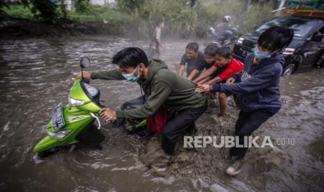 Pengendara menuntun kendaraannya yang mogok akibat banjir, ilustrasi