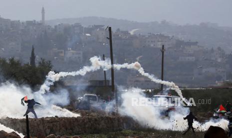 Warga Palestina mencari perlindungan dari gas air mata selama bentrokan yang meletus menyusul demonstrasi menentang permukiman Israel di tanah Desa Bet Dajan, dekat Kota Nablus, Tepi Barat, 16 Desember 2022. Menurut petugas medis Bulan Sabit Merah Palestina, setidaknya lima warga Palestina terluka dalam bentrokan.