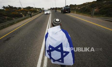 Pengunjuk rasa mengenakan bendera Israel saat pendukung sayap kanan Israel berbaris selama rapat umum di dekat pos terdepan ilegal Avitar, dekat kota Nablus di Tepi Barat, Senin (10/4/2023). Rapat umum tersebut bertujuan untuk melegitimasi pos terdepan Avitar, yang dibangun di atas tanah Israel. desa Beta dekat Nablus.