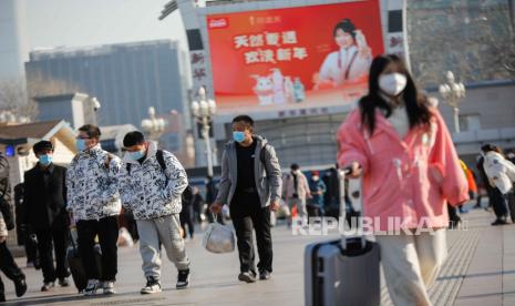 Passengers wearing face masks walk with their luggage in front of the Beijing Railway Station in Beijing, China, 10 January 2023. Chinese passengers are travelling domestically as the nation