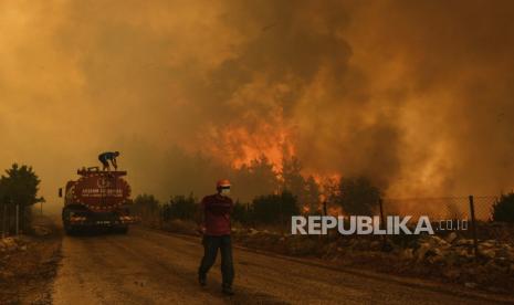  Seorang pria menyusuri jalan di desa Sirtkoy yang dilanda kebakaran, dekat Manavgat, Antalya, Turki, Minggu, 1 Agustus 2021. Lebih dari 100 kebakaran hutan telah dikendalikan di Turki, menurut para pejabat. Menteri kehutanan mentweet bahwa lima kebakaran terus berlanjut di tujuan wisata Antalya dan Mugla.