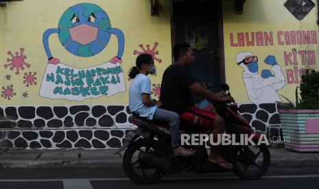 Pengendara motor melintas di depan mural tentang Covid-19 (ilustrasi) 