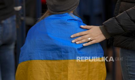 Seorang wanita meletakkan tangannya di punggung seorang anak yang terbungkus bendera Ukraina selama protes terhadap perang Rusia di Ukraina, di depan kedutaan Rusia di Bucharest, Rumania, beberapa waktu lalu.