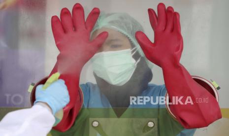  Seorang pekerja medis dibantu oleh seorang kolega untuk menyemprotkan sarung tangan karet dengan disinfektan di lokasi uji virus Corona di Laboratorium Genomik Solidaritas Indonesia di Jakarta, Indonesia, Senin, 14 Desember 2020. 