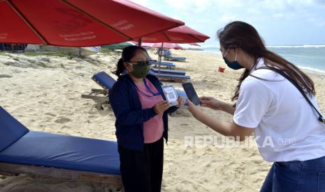 Pengunjung melakukan transaksi pembayaran berbasis digital dengan pedagang pantai menggunakan Quick Response Code Indonesian Standard (QRIS) di Pantai Pandawa, Badung, Bali, Sabtu (11/7/2020). Bank Indonesia bekerjasama dengan Bank Mandiri, pengelola kawasan serta pemerintah daerah setempat meresmikan Pantai Pandawa sebagai kawasan wisata pantai digital berbasis QRIS yang menyediakan sistem pembayaran non-tunai untuk memudahkan wisatawan serta meminimalisir terjadinya kontak fisik guna mencegah penyebaran COVID-19. 