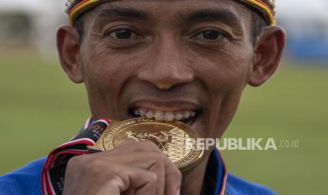 Pelari Jawa Barat Agus Suprayogo menggigit medali usai pengalungan medali nomor lari 10.000 meter putra PON Papua di Stadion Atletik Mimika Sport Center, Kabupaten Mimika, Papua, Selasa (12/10/2021). Agus meraih medali emas, sementara pelari Sulawesi Tengah Noveldi Petingko meraih medali perak dan pelari Kalimantan Barat Irmansyah meraih medali perunggu. 