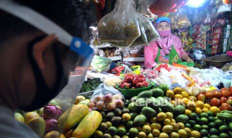 Penjual sayuran dan buah menggunakan masker dan alat pelindung wajah saat melayani pembeli di pasar tradisional. ilustrasi