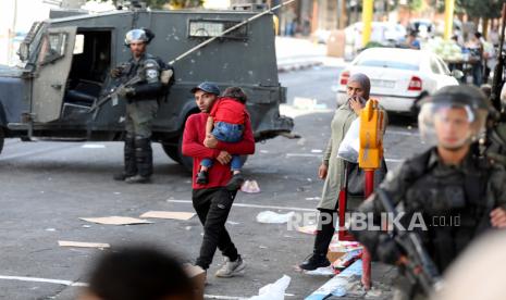  Warga Palestina berjalan melewati tentara Israel selama bentrokan dengan pengunjuk rasa Palestina di kota Hebron, Tepi Barat, 12 Oktober 2022. 