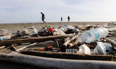 Orang-orang berjalan-jalan di sepanjang pantai yang dipenuhi sampah plastik (ilustrasi).