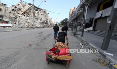 Seorang anak laki-laki Palestina menarik gerobak yang membawa saudara laki-lakinya dan barang-barang mereka saat mereka melarikan diri dari rumah mereka selama serangan udara dan artileri Israel, di dekat lokasi gedung menara yang hancur dalam serangan sebelumnya di Kota Gaza.