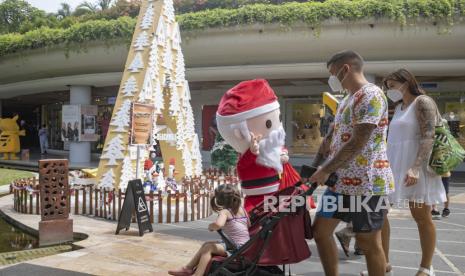  Wisatawan yang memakai masker wajah berjalan melewati pria berpakaian Santa Claus di Kuta, Bali, Indonesia, 23 Desember 2020. Untuk mengantisipasi lonjakan kasus COVID-19 saat libur Natal dan Tahun Baru, pemerintah Bali memperketat protokol kesehatan di beberapa kawasan wisata.