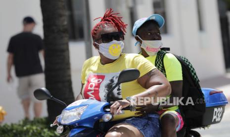 Orang-orang yang memakai masker pelindung naik skuter ke Ocean Drive selama pandemi coronavirus, Minggu, 12 Juli 2020, di Miami Beach, Florida. 