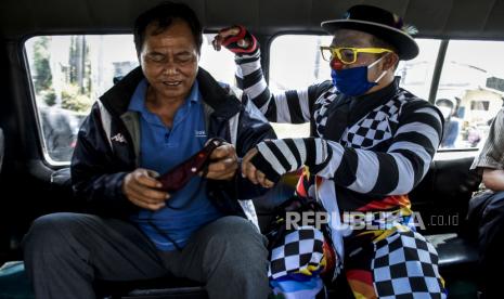 Anggota Badut Nyentrik Cimahi Bandung Sauyunan (Necis) membagikan masker kain gratis kepada penumpang angkot di Jalan Raya Simpang, Padalarang, Kabupaten Bandung Barat.