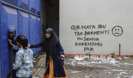 Pemuda berdiri di depan gerbang masuk Stadion Kanjuruhan, yang dinding temboknya tertera tulisan: air mata ibu tak berhenti, itu semua karenamu pak. (ilustrasi) 