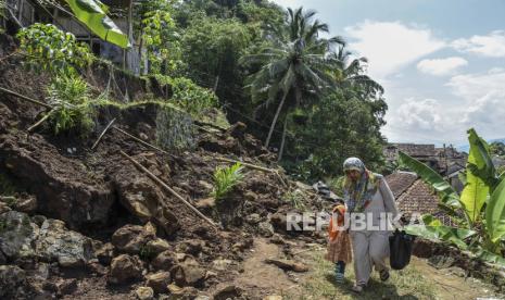 Warga berjalan melintasi material tanah longsor yang menimbun jalan dan rumah di Desa Banyurasa, Kabupaten Tasikmalaya, Jawa Barat, Kamis (4/5/2023). 