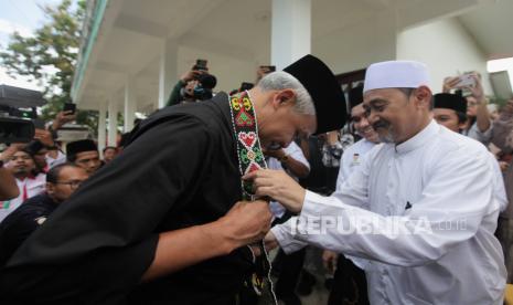 Calon Presiden nomor urut tiga Ganjar Pranowo (kiri) dikalungi kain oleh pengasuh Pondok Pesantren Syaichona Cholil, Balikpapan, Kalimantan Timur, Selasa (5/12/2023). Pada kunjungan tersebut Ganjar Pranowo bersilaturahmi dengan ulama pondok pesantren menjelang Pilpres 2024.