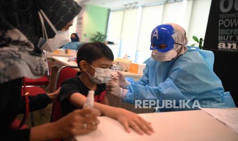 Tenaga kesehatan mengenakan topeng superhero saat menyuntikkan vaksin COVID-19 dosis kedua kepada seorang anak di Jakarta. Meski laju vaksinasi anak masih rendah PTM 100 persen tetap diputuskan berjalan.