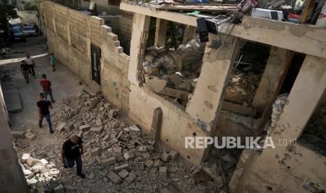 Warga Palestina berjalan melewati rumah yang rusak di kamp pengungsi Jenin di Tepi Barat, Rabu, (5/7/2023).