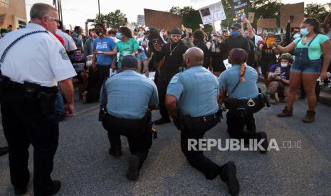 Petugas polisi dari Ferguson, Mo, berlutut dan bergabung dengan pengunjuk rasa aksi menyerukan keadilan atas kematian George Floyd di tempat parkir kantor polisi, Sabtu (30/5). Demonstrasi itu dipicu oleh kematian Floyd, seorang pria kulit hitam yang terbunuh ketika ditahan polisi di Minneapolis pada 25 Mei