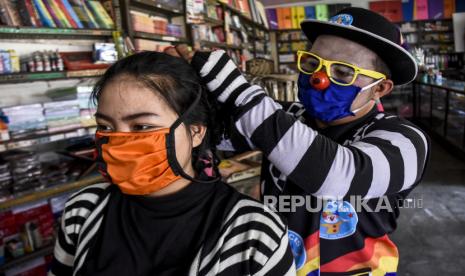 Anggota Badut Nyentrik Cimahi Bandung Sauyunan (Necis) memasangkan masker kepada karyawan di salah satu toko di kawasan Alun-alun Cimahi, Kota Cimahi, Selasa (14/4). Komunitas Badut Necis membagikan 2020 masker kain secara gratis kepada pengendara, sopir, pedagang serta masyarakat yang memerlukan sebagai salah satu bentuk keprihatinan sekaligus berpartisipasi dalam upaya meminimalisir penyebaran virus Corona (Covid-19)