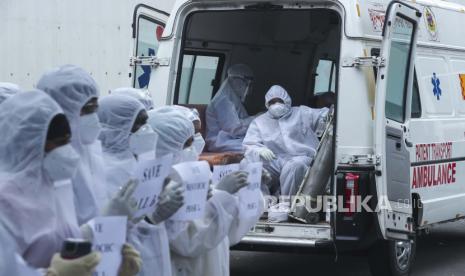 Petugas kesehatan yang duduk di ambulans menonton pekerja kesehatan kontrak dalam pakaian pelindung diri memegang plakat selama protes di pusat COVID-19 Nesco Jumbo di Mumbai, India Senin (5/7). Para pekerja kesehatan memprotes setelah mereka dikeluarkan pemberitahuan penghentian dari pekerjaan mereka dengan segera.