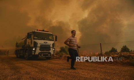  Seorang pria berlari, di desa Sirtkoy yang dilanda kebakaran, dekat Manavgat, Antalya, Turki, Minggu, 1 Agustus 2021. Lebih dari 100 kebakaran hutan telah dikendalikan di Turki, menurut para pejabat. Menteri kehutanan mentweet bahwa lima kebakaran terus berlanjut di tujuan wisata Antalya dan Mugla.