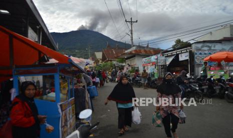 Warga membawa barang belanjaan berlatar belakang Gunung Marapi yang mengeluarkan abu vulkanik di Pasar Sungai Pua, Agam, Sumatera Barat, Ahad (21/4/2024). Petugas pos pengamatan gunung api (PGA) Marapi di Bukittinggi mencatat, aktivitas gunung yang berada pada status siaga level itu kembali meningkatserta mengimbau warga menjauh dari radius 4,5 kilometer dari pusat erupsi di kawah puncak Gunung Marapi. 