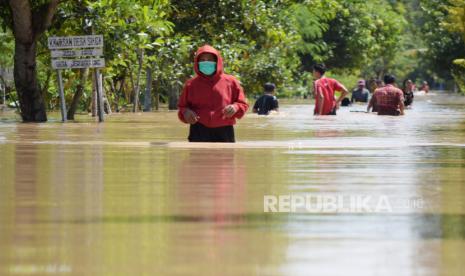 Sejumlah warga menerobos jalan yang terendam banjir di Desa Jerukgulung, Balerejo, Kabupaten Madiun, Jawa Timur, Kamis (15/4/2021). Sejumlah desa di empat kecamatan di Kabupaten Madiun terendam banjir luapan Sungai Jeroan akibat hujan deras Rabu (14/4) sore hingga malam. 