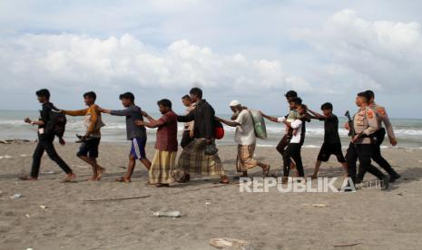 Personel Polri  dan TNI mengawal sejumlah imigran etnis Rohingya untuk dipindahkan ke lokasi penampungan usai terdampar di Desa Lampanah Leugah, Kecamatan Seulimeuem, Aceh Besar, Aceh, Kamis (16/2/2023). Sebanyak 62 orang imigran etnis Rohingya terdiri dari 23 orang laki-laki dewasa, 21 orang perempuan dewasa dan 18 orang anak-anak terdampar di pantai Desa Lampanah Leugah, Kabupaten Aceh Besar.  