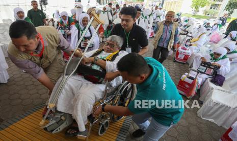 Petugas membantu mendorong kursi roda jamaah haji lansia. 