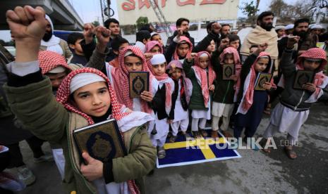 Anak-anak dari pendukung partai Liga Muslim Markazi Pakistan memegang Alquran saat mereka berdiri di atas bendera Swedia saat melakukan demo terhadap Swedia di Peshawar, Pakistan, Selasa (24/1/2023).