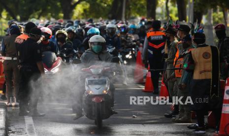 Polisi berpakaian adat menyemprotkan larutan disinfektan ke kendaraan bermotor yang memasuki Surabaya di pintu keluar Jembatan Suramadu, Surabaya, Jawa Timur, Senin (20/4/2020). Kegiatan itu untuk menghambat dan memutus penyebaran COVID-19