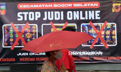 Warga berjalan di depan spanduk sosialisasi larangan judi online di Kantor Kecamatan Bogor Selatan, Kota Bogor, Jawa Barat, Senin (1/7/2024).