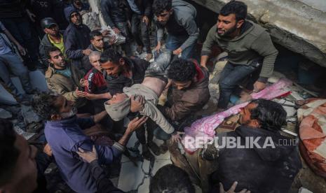 Warga Palestina menyelamatkan seorang anak laki-laki yang terluka di antara puing-puing rumah yang hancur akibat serangan udara Israel di kota Deir Al Balah, Jalur Gaza selatan, (18/2/2024).